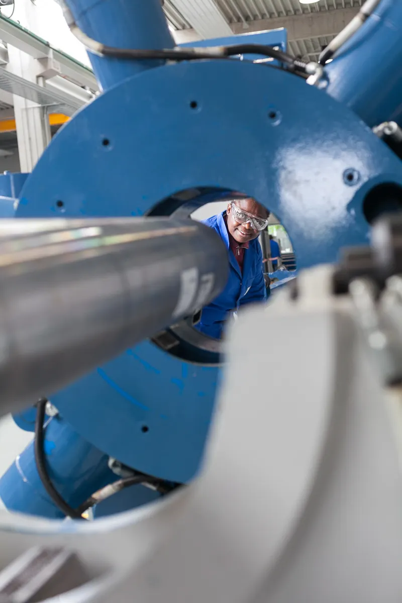 Mitarbeiterin in Arbeitskleidung kontrolliert eine große Industriemaschine durch eine runde Öffnung.
