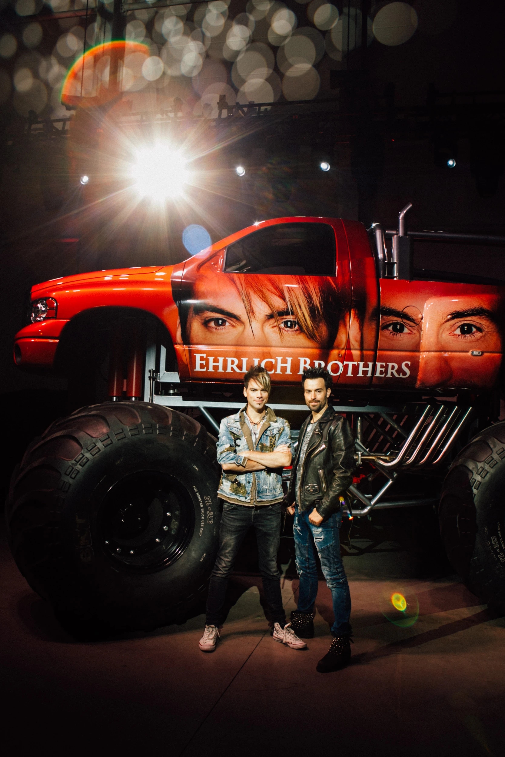 Die Ehrlich Brothers vor ihrem roten Monstertruck mit großformatigen Porträts der beiden auf der Fahrzeugseite.