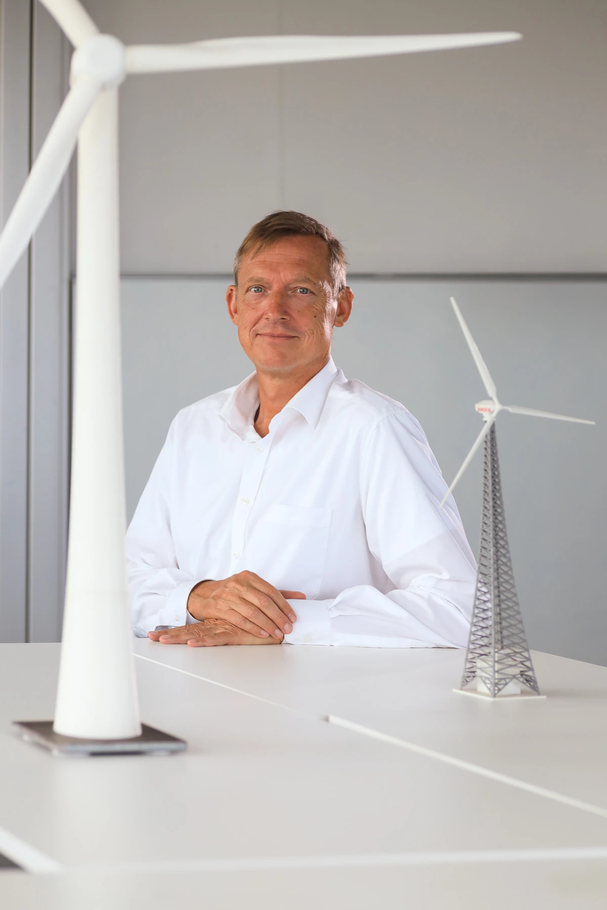 Portrait im Bereich Windenergie: Mann im weißen Hemd zwischen Modellen von Windkraftanlagen auf einem Tisch.