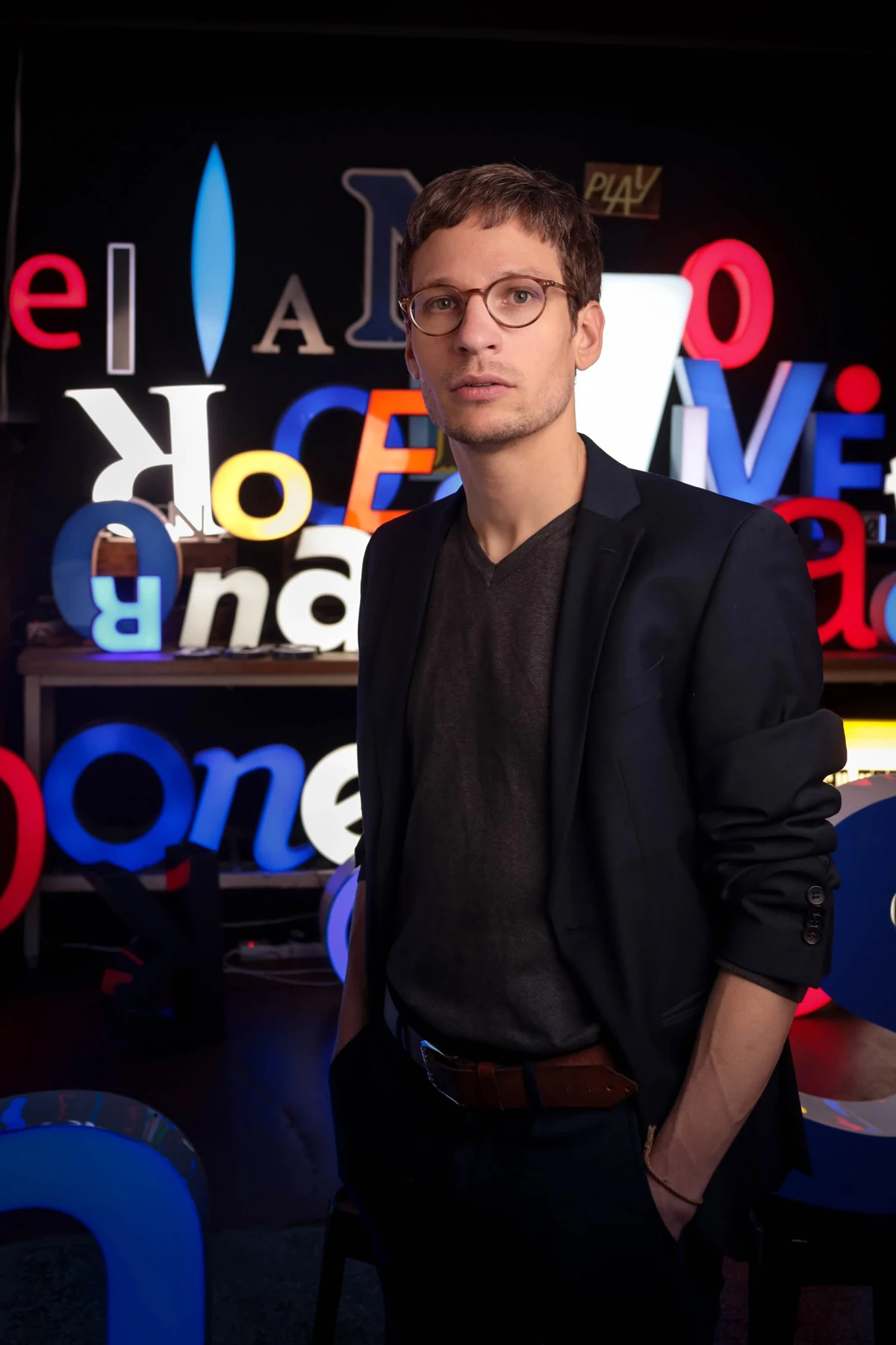 Portrait des Sprachwissenschaftlers Dr. François Conrad vor einer Wand mit bunten Leuchtbuchstaben.